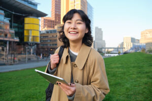 Happy young brunette girl, asian woman walks around city with tablet, goes to university with her digital gadget and backpack.